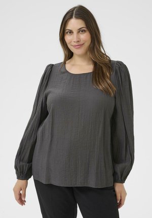 Parte superior texturizada en gris con mangas largas abullonadas y escote redondo. La tela presenta un sutil patrón arrugado. Combinado con pantalones negros.
