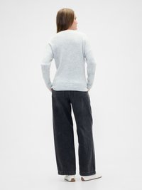Suéter gris claro, de corte holgado, con puños y dobladillo acanalados. Combinado con pantalones de mezclilla oscuros de pierna ancha. Diseño sencillo, look casual.
