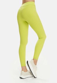 Leggings de culoare verde lime, confecționate dintr-un material elastic, cu talie înaltă și un design fără cusături, asortate cu pantofi sport de culoare deschisă.