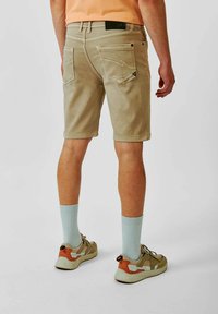 Beige shorts met achterzakken, rechte snit en zichtbare stiksels. Draag ze met muntgroene sokken en neutrale sneakers.