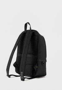 Μαύρο σακίδιο με επενδεδυμένη πλάτη και ρυθμιζόμενους ιμάντες ώμου, εμφανιζόμενο από πίσω σε απλό ανοιχτό φόντο.