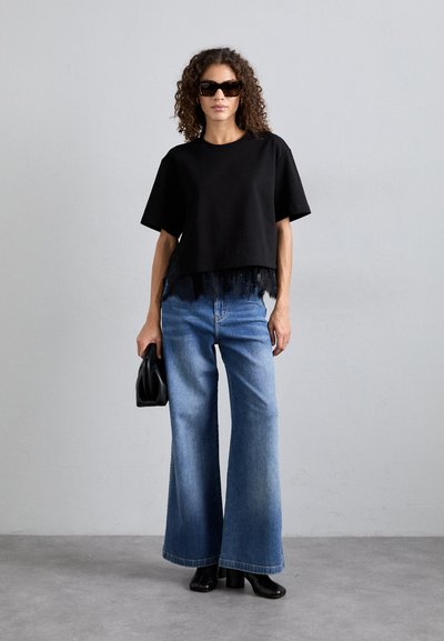 Juoda trumpa marškinėliai su nėriniu, derinami su šviesiai mėlynomis plačiomis kelnėmis. Modelis laiko juodą rankinę, dėvi tamsius akinius nuo saulės.