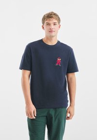 Camiseta de algodón de manga corta en color azul marino con un pequeño diseño bordado colorido en el lado izquierdo del pecho. Cuello plano y corte relajado.
