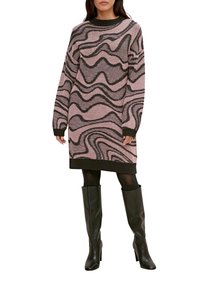 Robe pull tricotée en rose clair avec des motifs ondulés sombres, dotée de manches longues et d'un col côtelé, associée à des bottes noires montantes.