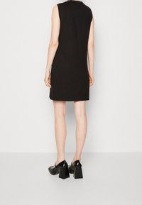 Abito nero senza maniche con una texture a coste, vestibilità aderente e orlo dritto. Abbinato a scarpe nere con tacco a blocco.