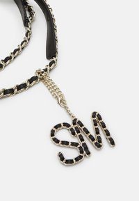Black chain strap with gold hardware, featuring a "SM" pendant made of interlinked black and gold chain links. Smooth texture.