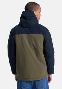 Vandafvisende jakke med hætte og øverste del i navy blå og nederste del i olivengrøn. Tekstureret stof med en afslappet pasform.