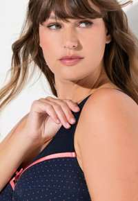 Mörkblå bh med rosa prickar och detaljer. Har tunna band och en rosett, mjuk tygtextur och en smidig design.