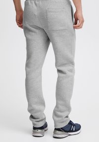 Graue Sweatpants mit schmaler Passform aus weichem Stoff. Sie verfügen über eine Gesäßtasche und gerippte Bündchen an den Knöcheln, kombiniert mit blauen Sneakers.