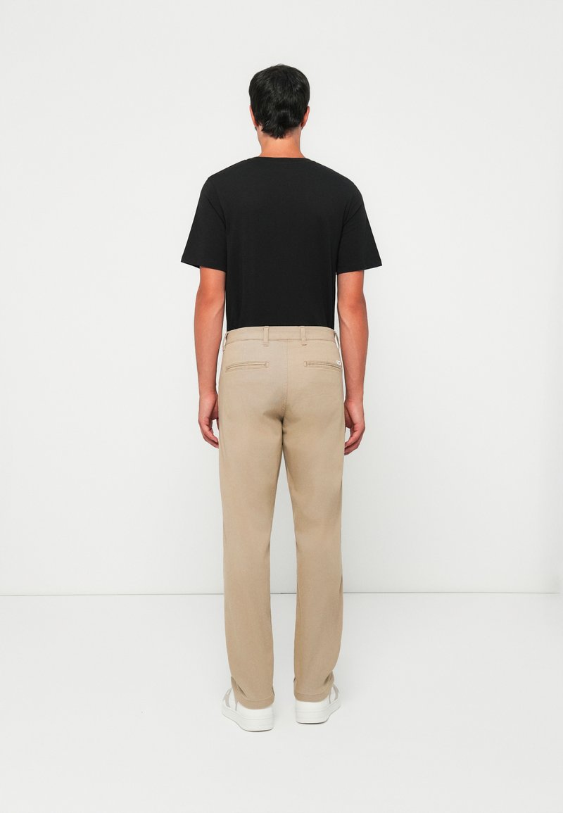 T-shirt noir à manches courtes associé à un pantalon beige clair. La tenue présente un design minimaliste avec des coupes droites et sans motifs visibles.