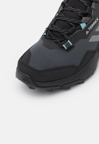 Czarne buty sportowe z teksturowaną cholewką, szarymi akcentami, turkusowymi sznurówkami i wytrzymałą podeszwą, odpowiednie do aktywności na świeżym powietrzu.