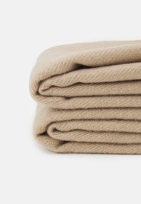 Beige vevd teppe, brettet i tre deler. Mykt, teksturert stoff med et fint strikkemønster. Naturlig farge, minimalistisk design.