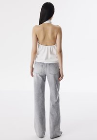 Top bianco senza maniche con sottili righe, abbinato a jeans a gamba larga in denim chiaro con dettagli decorativi nel tessuto.