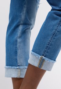 Jeans aus Denim mit einem zweifarbigen Design; oben am Oberschenkel dunkler und an den Säumen heller. Die Säume sind mit offenen Nähten verziert und haben einen umgeschlagenen Saum.