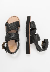 Schwarze, geflochtene Ledersandalen mit flacher Sohle, versehen mit gekreuzten Riemen und einer Schnallenverschluss. Strukturierte Oberseite und glattes Innenfutter.