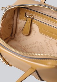 Borsa a tracolla in pelle marrone aperta per mostrare la fodera in tessuto con marchio e la tasca interna con zip dotata di linguetta in pelle coordinata.