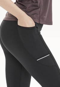 Svarta leggings med sidoficka och vit accentrand. Tillverkade av stretchigt material, med figursydd design och platta sömmar.