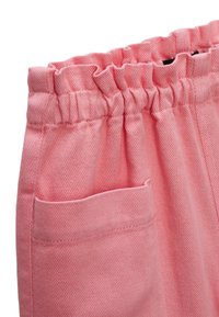 Pantalon en coton rose avec une taille élastique, des détails froncés et une poche sur le côté. Le tissu a une apparence texturée et tissée.