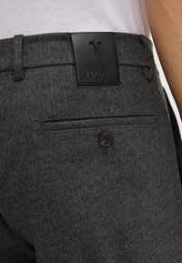 Grau ma�ßgeschneiderte Hosen aus strukturiertem Stoff, mit einem schwarzen Leder-Logo-Patch und einem kleinen Knopfdetail auf der hinteren Tasche.