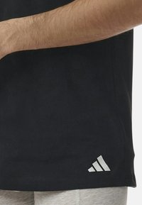 Svart bomullströja med korta ärmar, med en vit Adidas-logotyp accentuerad vid fållen. Slät textur och regular fit.