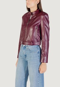 Veste en cuir bourgogne au design ajusté, col mandarin, fermeture éclair à l'avant et poches latérales. Associée à un jean en denim bleu clair.