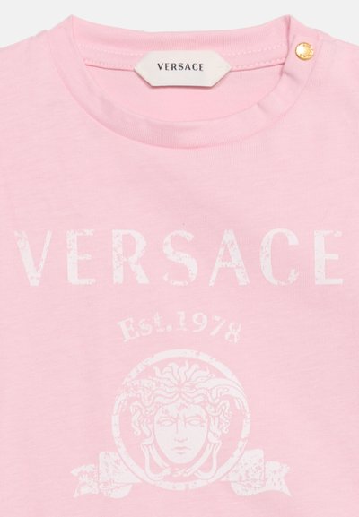 Ροζ πουκάμισο Versace με λευκό ξεθωριασμένο λογότυπο κεφαλής Μέδουσας, κείμενο "VERSACE", "Est. 1978" από κάτω και ένα χρυσό κουμπί κοντά στον γιακά.