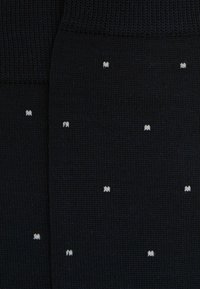 Sorte sokker med en strikket tekstur, prydet med små hvide prikker. Designet er ensartet og diskret på stoffet.