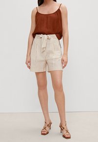 Haut sans manches marron associé à un short taille haute beige à rayures avec une ceinture nouée. Le mannequin porte des sandales à talons bronze à lanières.