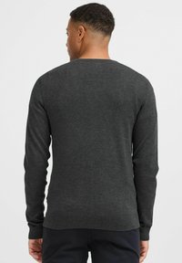 Grå strikket sweater med lange ærmer, rund halsudskæring og ribbede manchetter. Glat tekstur med en tætsiddende kant. Ingen markante mønstre eller accenter.