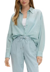 Camicia azzurra chiara, botton-up, in un tessuto leggero con un grande colletto e maniche lunghe, abbinata a pantaloni a vita alta azzurri chiari coordinati.
