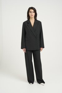 Completo a righe verticali nere con giacca doppiopetto e pantaloni a gamba larga. Presenta un design su misura, righe contrastanti e dettagli di scarpe bianche a punta.
