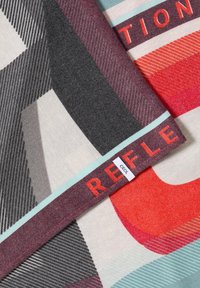 Multicolored textile featuring geometric patterns in grey, red, and teal. Includes a label with "Cecil" and accents in contrasting colors.