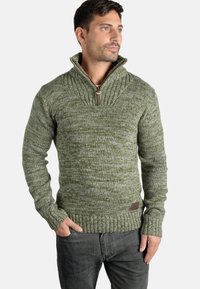Jersey verde de punto con un cuello alto, que cuenta con un cierre de media cremallera y puños acanalados. Tejido texturizado con un patrón moteado.