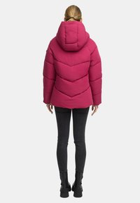Fuchsia pufferjack met een capuchon, voorzien van een chevron-quiltontwerp, gedragen over donkere skinny jeans en zwarte enkellaarsjes.