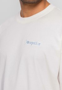 Lysbeige t-shirt lavet af bomuld; har en rund halsudskæring og korte ærmer; med broderet "Dropsize" logo i lyseblå.