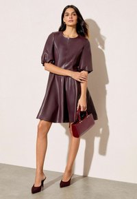 Bordová šaty z imitácie kože s krátkymi puff rukávmi a rozšírenou sukňou. V kombinácii s ladacou kabelkou a topánkami na ihlovom podpätku.