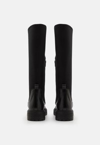 Botas negras hasta la rodilla con un cuero liso en la parte inferior y un tejido texturizado en la parte superior, con tiradores laterales dobles y suelas de goma resistentes.