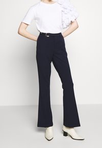 Valkoinen t-paita, jossa on röyhelöinen hiha, yhdistettynä laivastonsinisiin liehuviin housuihin. Asussa on vyö, jossa on pyöreä solki, sekä valkoiset nilkkurit.