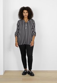 Black and white striped long-sleeve blouse with a V-neck and button detail, paired with black slim-fit pants and black shoes.