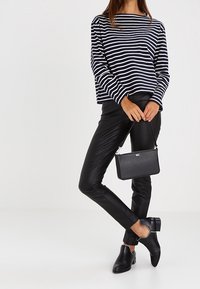 Stribet top i sort og hvid med lange ærmer, parret med sorte læderbukser og ankelstøvler; holder en lille sort tekstureret håndtaske.