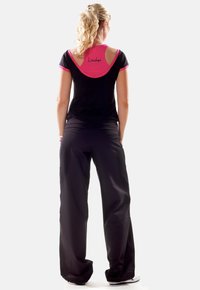 Black athletic top with pink accents, round neckline, and cut-out detail on shoulders, paired with loose black pants, viewed from the back.