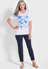 Witte korte mouwen t-shirt met een blauwe bloemenprint, gecombineerd met marineblauwe slim-fit broek en lichte sandalen. Glad stof en relaxte pasvorm.