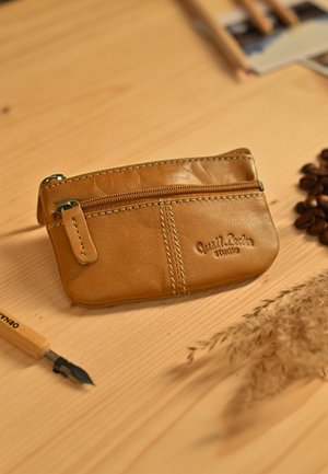 Tarjetero de cuero color marrón con un bolsillo con cremallera, detalles cosidos y marca en relieve. Forma compacta y rectangular.