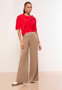 Red short-sleeve sweater with a tie detail at the neck, paired with high-waisted, beige wide-leg trousers; smooth fabric and clean lines.