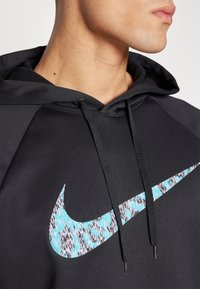 Juodas Nike megztinis su kapuce, kuriame yra turkio ir juodos spalvos raštuotas swoosh logotipas, su raišteliu ir glotnia tekstūra.