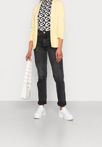 Blazer amarillo, blusa de patrón blanco y negro, jeans oscuros de tiro alto, zapatillas blancas y un bolso blanco con agujeros decorativos.
