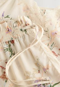 Tissu à motifs floraux en beige doux avec des détails froncés et une bordure en dentelle. Présente des couleurs pastel délicates et des motifs naturels.