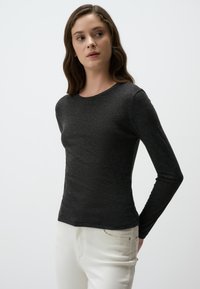 Langärmliges, eng anliegendes schwarzes Shirt aus weichem, strukturiertem Stoff mit rundem Halsausschnitt, kombiniert mit hellen Jeans.