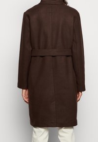 Manteau en laine marron à coupe droite, taille ceinturée, col haut, avec des détails de couture minimalistes à l'arrière. Texture lisse, design mi-long.