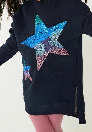 Sweat-shirt bleu marine orné de grands motifs d'étoiles en sequins multicolores turquoise et rose, avec une fermeture éclair latérale au niveau de l'ourlet.